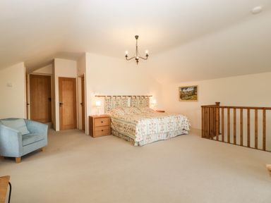 A bedroom with a double bed nightstands armchair and wooden railing at Timber Barn in Eardisland