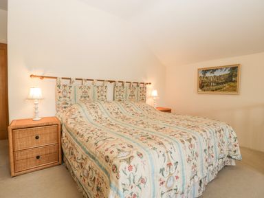 A bedroom with a patterned bedspread on the bed two bedside tables with lamps and a framed painting on the wall at Timber Barn in Eardisland