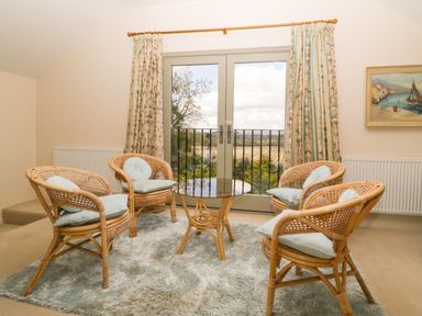 A sitting area with four rattan chairs and a glass table on a rug in front of patio doors at Timber Barn in Eardisland