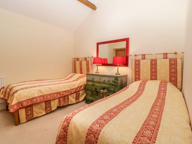 A bedroom with two single beds a chest of drawers with a decorative landscape painting two red lamps and a red framed mirror at Timber Barn in Eardisland