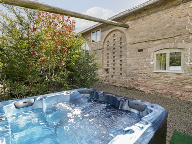 An outdoor hot tub with bubbling water near a stone building and trees at Timber Barn in Eardisland