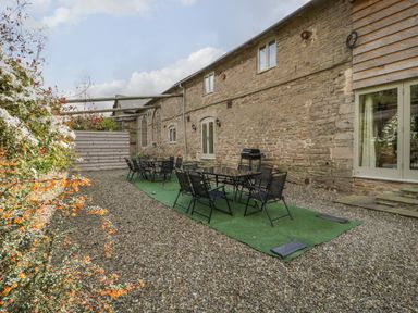 An outdoor patio area with two glass tables and multiple black chairs on a green mat beside a stone building at Timber Barn in Eardisland