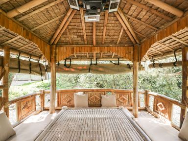 A bamboo gazebo with cushioned seating and a thatched roof surrounded by greenery at Timber Barn in Eardisland