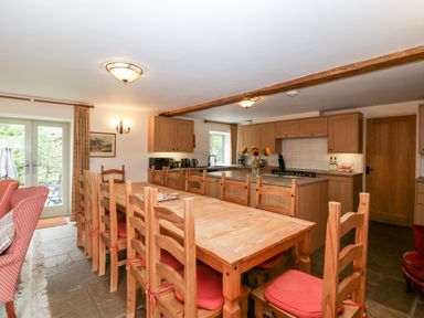 A kitchen and dining area with a long wooden table and wooden chairs with red cushions at Timber Barn in Eardisland