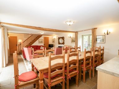 A dining area with a long wooden table and chairs with red cushions next to a living area with sofas and armchairs at Timber Barn in Eardisland