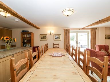 A dining room with a long wooden table and chairs a vase with sunflowers a bookshelf and a red armchair at Timber Barn in Eardisland
