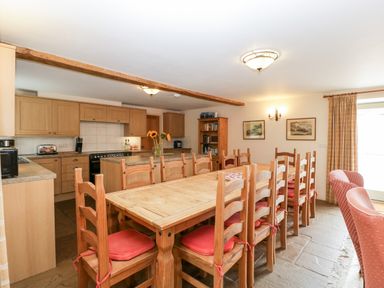 A kitchen and dining area with a long wooden dining table and chairs with red cushions at Timber Barn in Eardisland