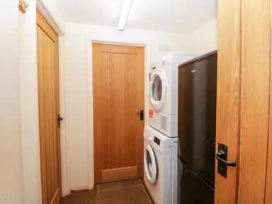 A utility room with stacked washing machine and dryer and a black refrigerator at Timber Barn in Eardisland