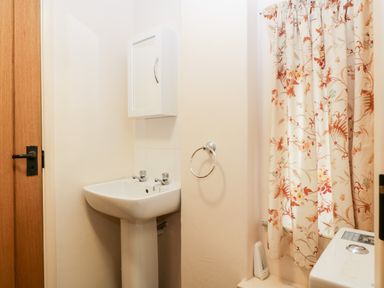A bathroom with a sink a towel ring a floral curtain and a washing machine at Timber Barn in Eardisland