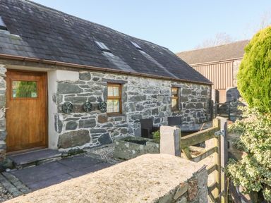 A stone building with a wooden door and windows with outdoor seating behind a wooden gate at Beudy Bach in Y Felinheli