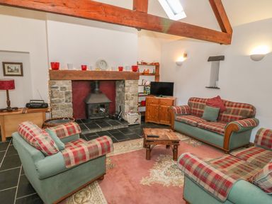 A living room with three plaid sofas around a wooden coffee table a stone fireplace exposed wooden beams and a television on a cabinet at Beudy Bach in Y Felinheli