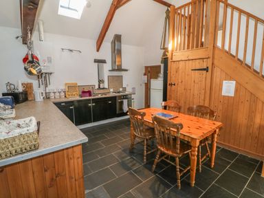 A kitchen with wooden cabinets a dining table with four chairs and a staircase at Beudy Bach in Y Felinheli
