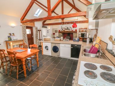 A kitchen with wooden dining table and chairs washing machine dishwasher stove and exposed wooden beams at Beudy Bach in Y Felinheli