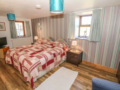 A bedroom with a double bed covered with a patchwork quilt two bedside tables with lamps two windows with curtains and a wooden floor at Beudy Bach in Y Felinheli
