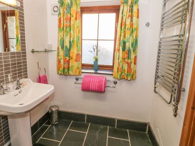 A bathroom with a sink radiator window with floral curtains and pink towels at Beudy Bach Y Felinheli