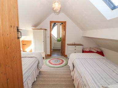 A bedroom with two single beds a wardrobe a chest of drawers and a round rug at Beudy Bach in Y Felinheli