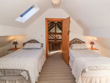 A bedroom with two single beds and nightstands with lamps through an open wooden door at Beudy Bach in Y Felinheli