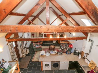 A kitchen area with countertop and hanging pots overlooking a living space with armchairs and rugs at Beudy Bach in Y Felinheli