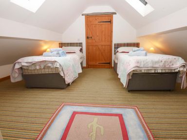 A bedroom with two beds and a wooden door at Beudy Mawr Y Felinheli