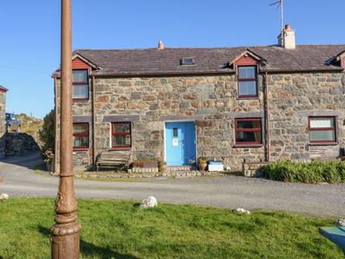 A stone house with a blue door and red window frames next to a gravel path and green grass at Hendre in Y Felinheli