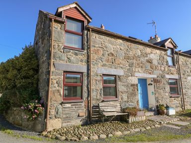 A stone cottage with a blue door a bench and potted plants outside at Hendre in Y Felinheli