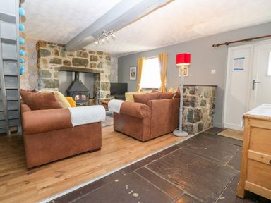 A living room with brown sofas facing a stone fireplace with a wood stove a red floor lamp wooden floor and a window with yellow curtains at Hendre in Y Felinheli