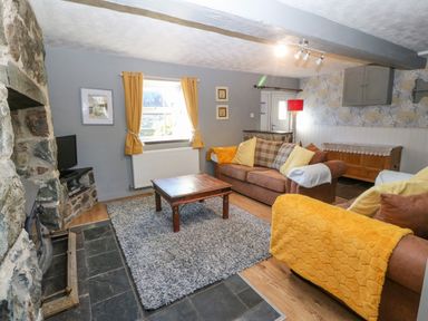 A living room with two brown sofas yellow cushions and throws a wooden coffee table stone fireplace and a window with yellow curtains at Hendre in Y Felinheli