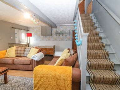A living room with two brown sofas and a staircase with patterned carpet at Hendre in Y Felinheli