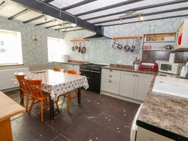 A kitchen with a table and four wooden chairs pots and pans hanging on the wall and kitchen appliances at Hendre in Y Felinheli