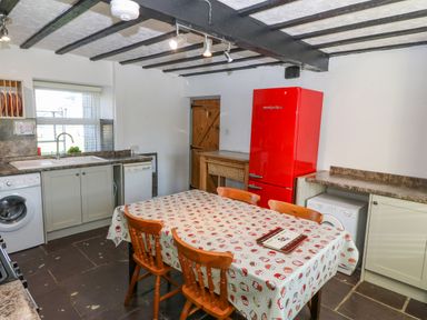 A kitchen with a wooden dining table with chairs a red refrigerator washing machines under counters and a window at Hendre in Y Felinheli