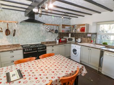 A kitchen with stove oven washing machine dishwasher and table with chairs at Hendre in Y Felinheli