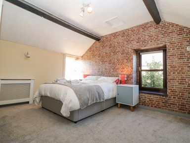 A bedroom with a bed a bedside table with a lamp a window and exposed brick walls at Hendre in Y Felinheli