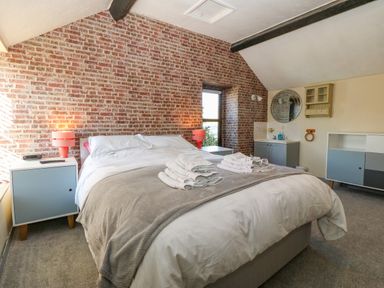 A bedroom with a bed towels on the bed lamps on bedside tables and a brick wall at Hendre in Y Felinheli
