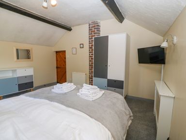A bedroom with a bed covered with a blanket and towels a wardrobe a television a dresser and a wooden door at Hendre in Y Felinheli