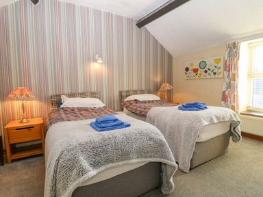 A bedroom with two single beds bedside tables and lamps next to a window at Hendre in Y Felinheli