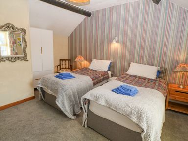 A bedroom with two single beds with blankets and folded towels bedside tables lamps a wardrobe and a chair at Hendre in Y Felinheli