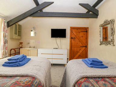 A bedroom with two single beds towels on the beds a wooden door a white dresser a sink and a wall mounted TV at Hendre in Y Felinheli