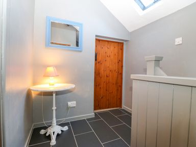 A hallway with a round table holding a lamp next to a wooden door and a blue framed mirror on the wall at Hendre in Y Felinheli