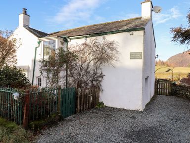 Exterior view of a white house with two chimneys a green gate gravel driveway and surrounding vegetation at Castle Lodge in Borrowdale
