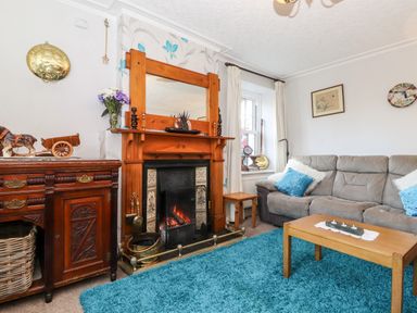 A living room with a fireplace wooden furniture blue rug and gray sofa at Castle Lodge in Borrowdale