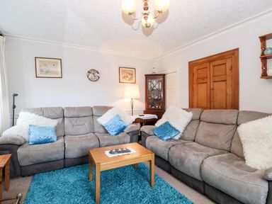 A living room with two gray sofas, a wooden coffee table, a blue rug, framed pictures on the wall, and a wooden cabinet at Castle Lodge in Borrowdale
