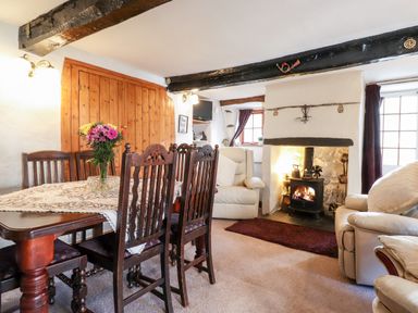 A dining area with a wooden table and chairs next to a living room with cream armchairs and a fireplace at Castle Lodge in Borrowdale