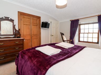 A bedroom with a bed covered in purple blanket and white towels a wooden dresser mirror a wooden chair window with purple curtains and wooden framed doors at Castle Lodge in Borrowdale