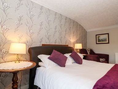A bedroom with a bed, side tables with lamps, and an armchair at Castle Lodge in Borrowdale