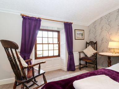 A bedroom with wooden chairs purple curtains and a round table with a lamp at Castle Lodge in Borrowdale