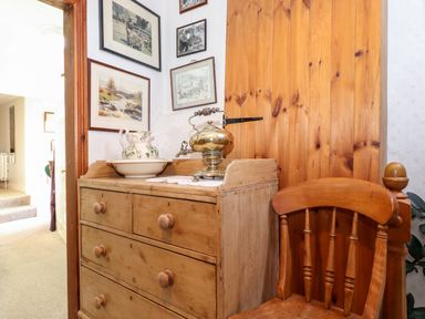 A wooden dresser with a ceramic pitcher and basin and a brass samovar next to a wooden chair and a wooden door at Castle Lodge in Borrowdale