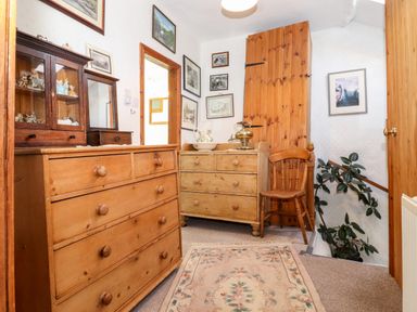 A hallway with wooden dressers and a chair along with framed pictures on the walls at Castle Lodge in Borrowdale