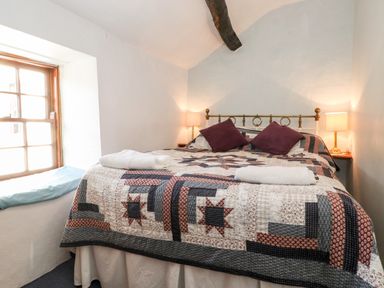 A bedroom with a double bed covered with a quilt and two purple pillows at Castle Lodge in Borrowdale