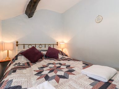 A bedroom with a patterned quilt on the bed two purple pillows folded towels on the bed and wooden beams on the ceiling at Castle Lodge in Borrowdale