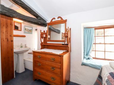 A bedroom with a wooden dresser with mirror a window with blue curtains and a white sink at Castle Lodge in Borrowdale